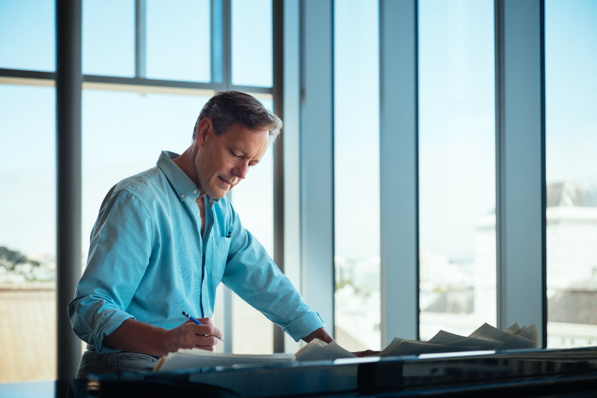 A man is focused on writing on a piece of paper with a pen in a well-lit room.